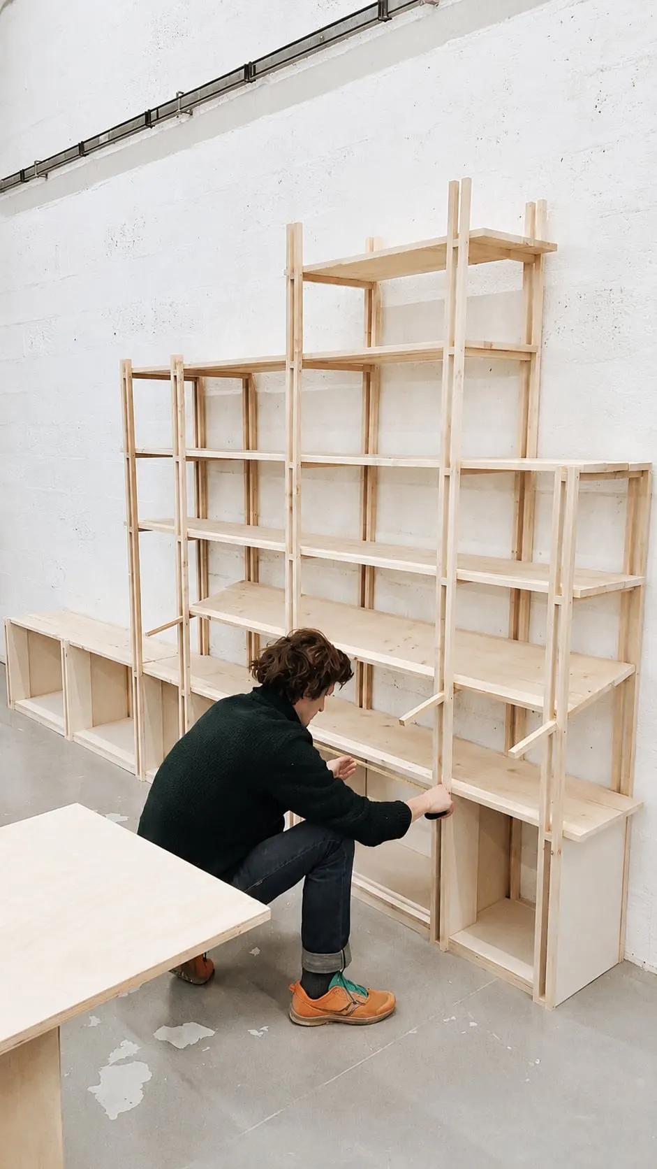 Bérenger assemble une bibliothèque en bois clair dans l’atelier