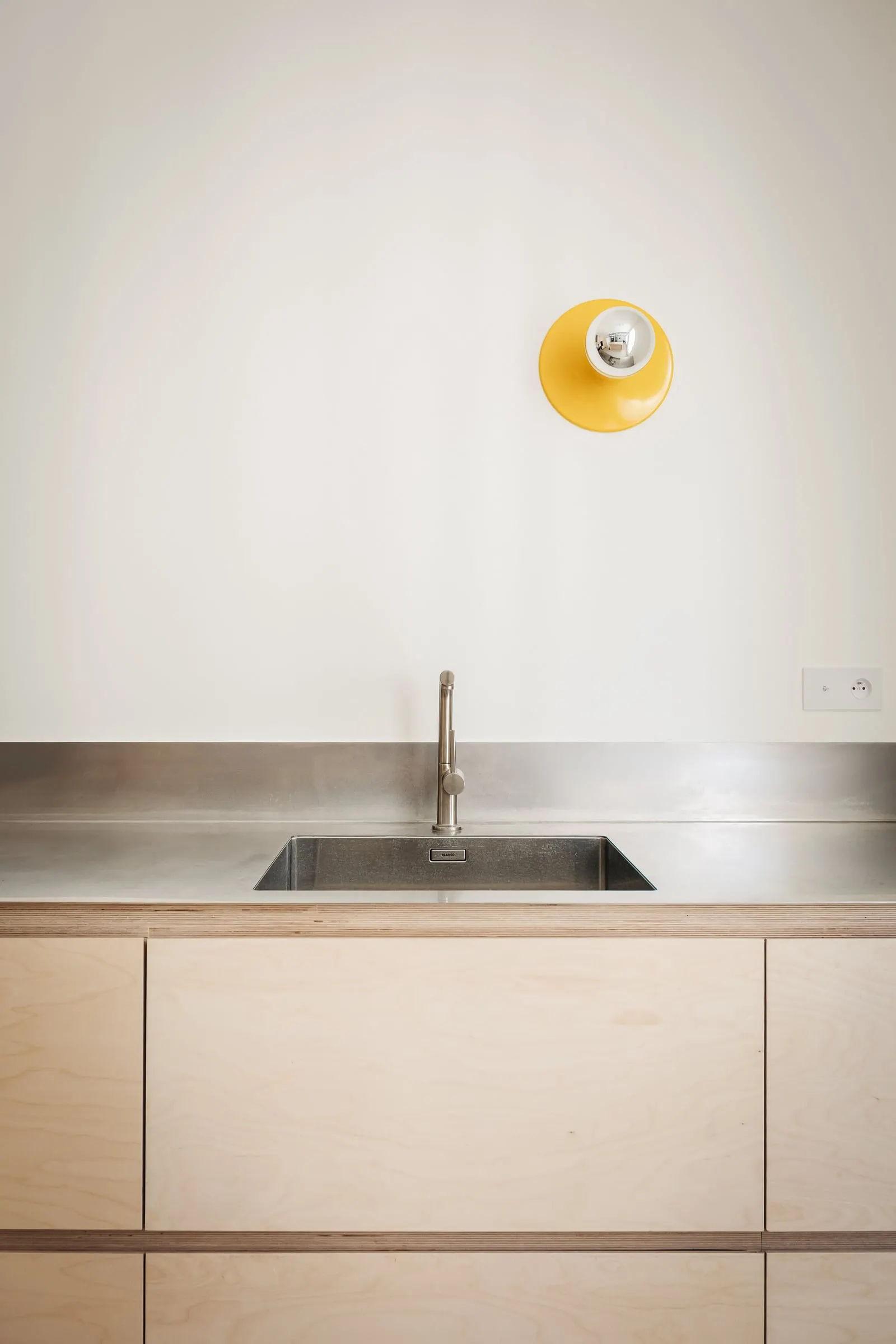 Plan de travail en inox et applique jaune sur mur blanc