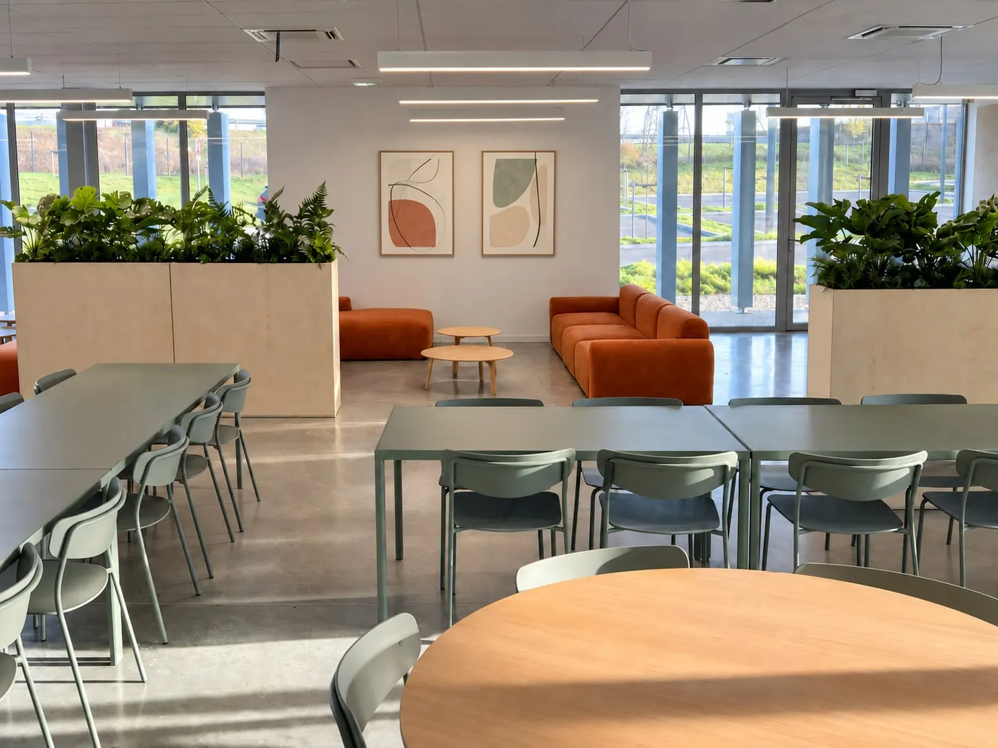 Cafétéria et coin détente aux canapés terracotta, séparés par des jardinières en bois