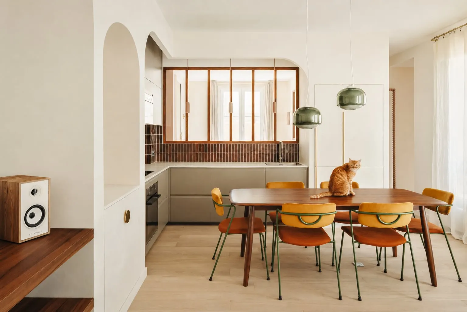 Salle à manger avec table en bois sombre et chaises jaunes, verrière en bois