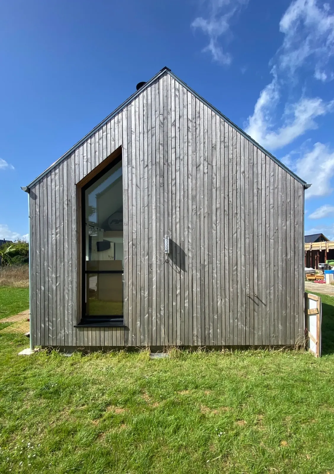 Pignon de la maison en bardage bois grisé par le temps, avec sa grande baie verticale